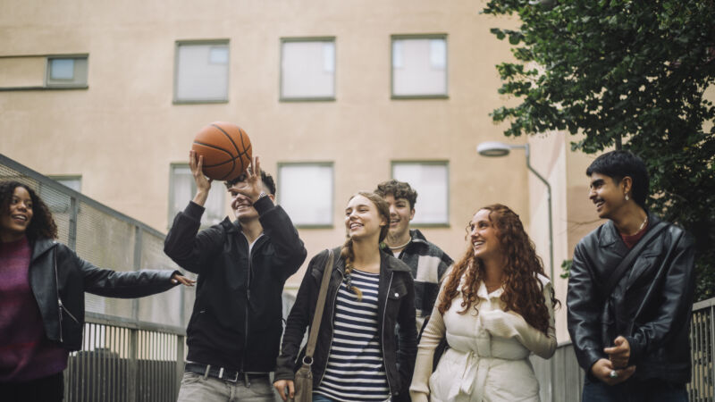 Glada elever som är ute och säljer med klassen och tittar på tonårskille som leker med basketbol