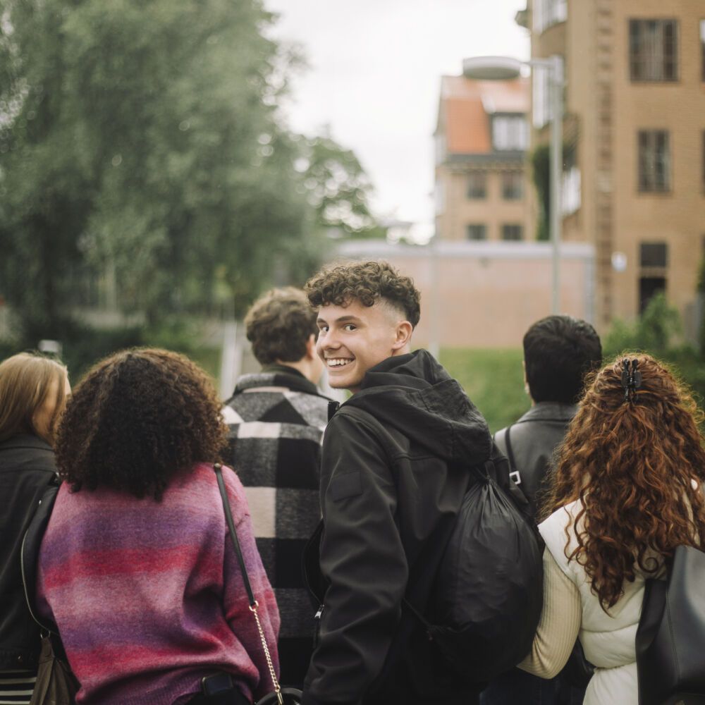 Porträtt av glad tonårskille som tittar bak gående med vänner och valt att sälja med klasskontots klassförsäljningsmodell som ger honom så hög vinst som möjligt.