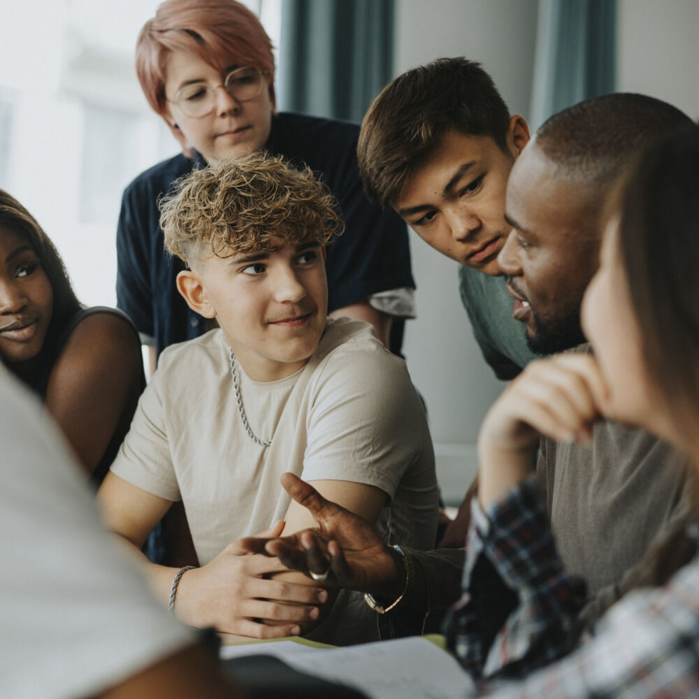 Tonåriga elever lyssnar på manlig lärare som pratar om klasskontots klassförsäljningsmodell med låg risk, mindre förtjänst